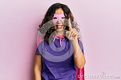 Middle age hispanic woman wearing super hero costume smiling with an idea or question pointing finger up with happy face, number Stock Photo