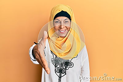 Middle age hispanic woman wearing traditional islamic hijab scarf smiling friendly offering handshake as greeting and welcoming Stock Photo