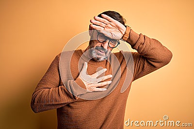 Middle age hoary man wearing brown sweater and glasses over isolated yellow background Touching forehead for illness and fever, Stock Photo