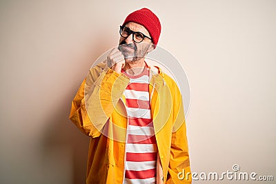 Middle age hoary man wearing glasses and rain coat standing over isolated white background with hand on chin thinking about Stock Photo