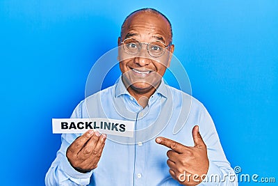 Middle age latin man holding paper with backlinks message smiling happy pointing with hand and finger Stock Photo