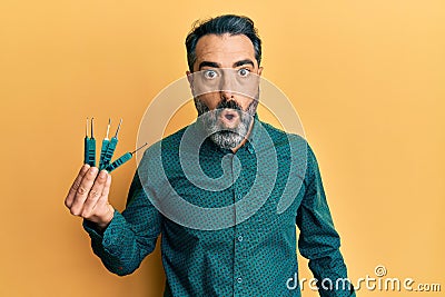 Middle age man with beard and grey hair holding picklock to unlock security door scared and amazed with open mouth for surprise, Stock Photo