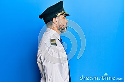 Middle age man with beard and grey hair wearing airplane pilot uniform looking to side, relax profile pose with natural face with Stock Photo