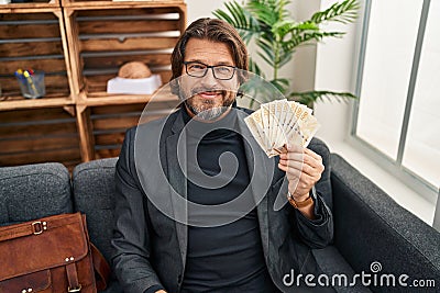 Middle age man psychologist holding denmark krone banknotes at psychology clinic Stock Photo