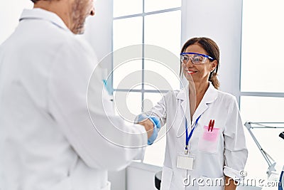 Middle age man and woman partners wearing scientist uniform shake hands at laboratory Stock Photo