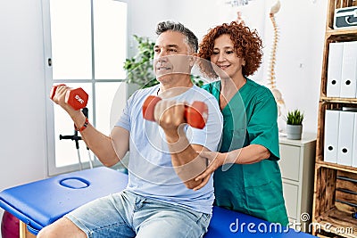 Middle age man and woman wearing physiotherapy uniform having rehab session using dumbbells at physiotherapy clinic Stock Photo