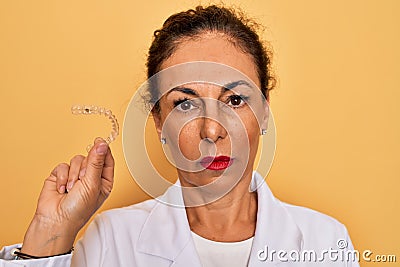 Middle age senior dentist woman holding clear aligner for teeth correction with a confident expression on smart face thinking Stock Photo