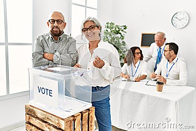 Middle age voter couple smiling happy putting vote in voting box at electoral center Stock Photo