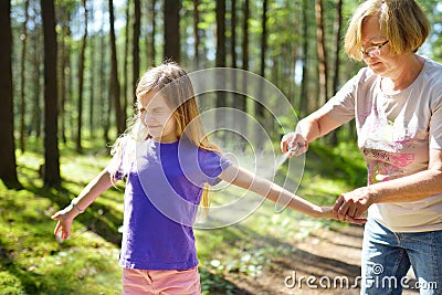 Middle age woman applying insect repellent to her granddaughter before forest hike beautiful summer day. Protecting children from Stock Photo