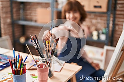 Middle age woman artist smiling confident holding paintbrushe at art studio Stock Photo