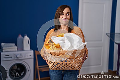 Middle age woman holding laundry basket at laundry room smiling looking to the side and staring away thinking Stock Photo