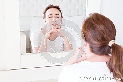 Middle age woman looking in mirror on face. Wrinkles and anti aging skin care concept. Selective focus Stock Photo