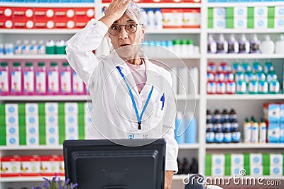 Middle age woman with tattoos working at pharmacy drugstore surprised with hand on head for mistake, remember error Stock Photo