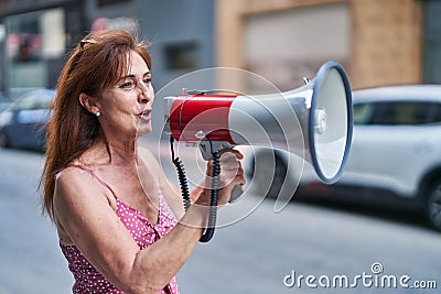 Middle age woman using megaphone speaking at street Stock Photo