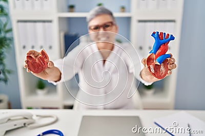 Middle age woman wearing doctor uniform holding heart ventricles at clinic Stock Photo