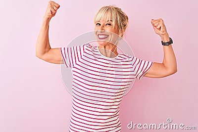 Middle age woman wearing striped t-shirt standing over isolated pink background showing arms muscles smiling proud Stock Photo