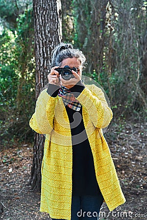 Woman makes photos with analog reflex camera looking at camera in forest Stock Photo
