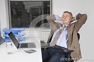 Middle-aged businessman resting on chair in front of laptop in office Stock Photo