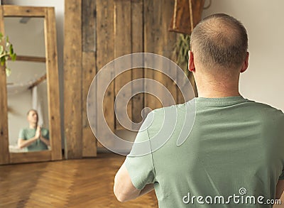 Middle-aged caucasian man practicing meditation, yoga near mirror with his reflection with wooden background with place for text Stock Photo