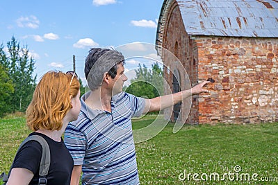 Middle aged dark-haired tourist man showing direction by hand for young redhead lady. Traveler asking path from stranger on Stock Photo