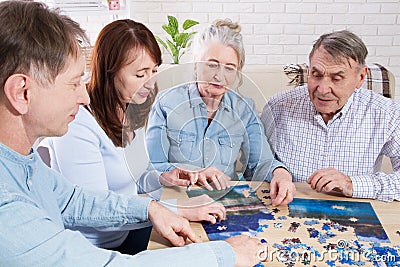 Middle-aged family elderly collects jigsaw puzzles at the table in the room Stock Photo