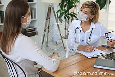 Middle aged female doctor therapist in medical mask on consultation with patient in office Stock Photo