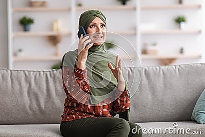 Middle-Aged Islamic Female Speaking By Phone Sitting At Home Stock Photo