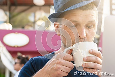 A middle-aged man in a blue hat is drinking coffee in front of a laptop. portrait close-up, looking into a mug. vertical photo Stock Photo