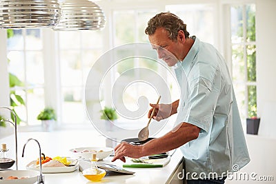 Middle Aged Man Following Recipe On Digital Tablet Stock Photo