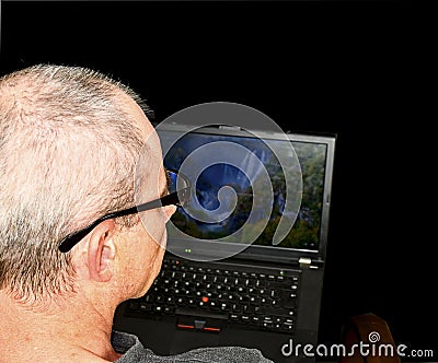 Middle aged man with glasses sitting in an armchair. Mature man using notebook on black background. Copy space. Senior Stock Photo