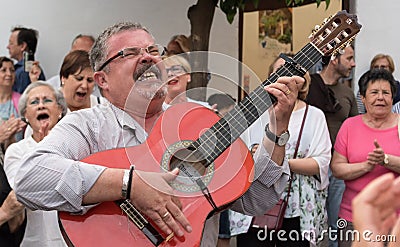 A middle-aged man singing folk songs and playing the guitar during a street concert of the folk choir in Cordoba during the festiv Editorial Stock Photo