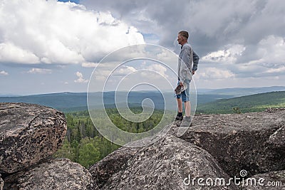 A middle-aged man at the top of the mountain enjoys a stunning view of the hilly valley. Freedom and goal achievement. Stock Photo