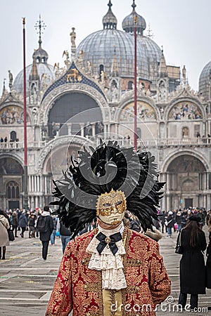 A middle-aged man in a vintage costume with a lace collar, wearing a carnival mask bordered by a circle of high black feathers Editorial Stock Photo