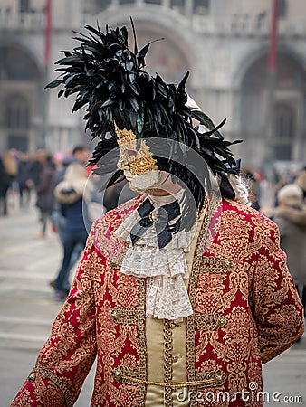 A middle-aged man in a vintage costume with a lace collar, wearing a carnival mask bordered by a circle of high black feathers Editorial Stock Photo