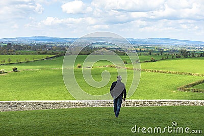 Middle-aged man walking in the field about to jump a wall, a stone fence. Overcome difficulties. Walk facing towards Editorial Stock Photo