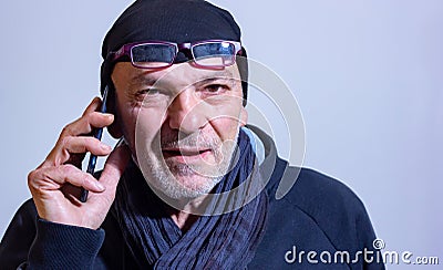 Middle-aged man with wool cap and glasses talking to a smartphone. Stock Photo