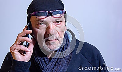 Middle-aged man with wool cap and glasses talking to a smartphone. Stock Photo