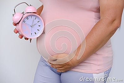 Middle-aged pregnant woman holds alarm clock near her belly close-up, waiting for newborn, concept of prenatal contractions, Stock Photo