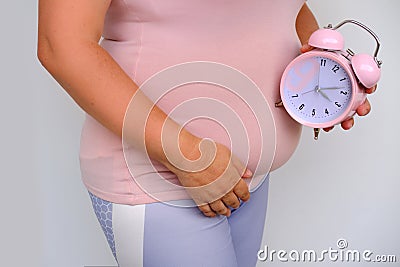 middle-aged pregnant woman holds alarm clock near her belly close-up, waiting for newborn, concept of prenatal contractions, Stock Photo