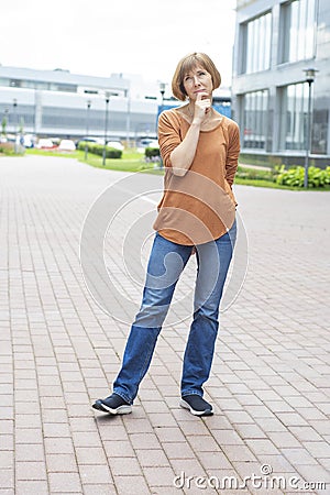 A middle-aged redhead woman in casual clothes stands in the street, lost in thought Stock Photo