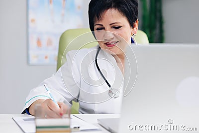 Middle aged senior head doctor in white medical coat sitting at workplace, talking to patient making video call on Stock Photo