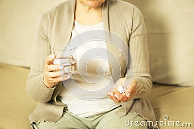 Middle aged unrecognized woman sitting at home, holding glas of fresh water and taking medicine. Stock Photo