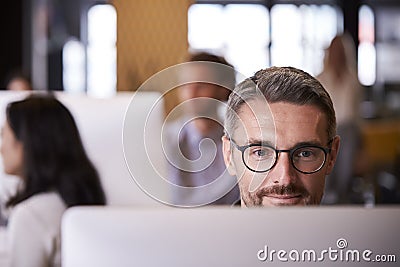 Middle aged white male creative using a computer in a busy office, selective focus, close up Stock Photo