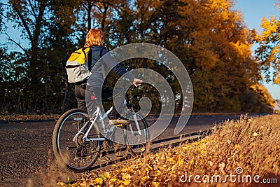 Middle-aged woman bicyclist riding in autumn field at sunset. Senior sportswoman admiring the view. Stock Photo