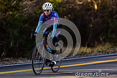 Middle aged woman cycling down a scenic road surrounded by trees during the Cedar Hill Race Festival Editorial Stock Photo