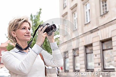 Middle-aged woman photographing through digital camera in city Stock Photo