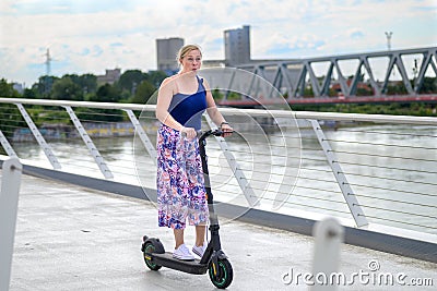 Middle-aged woman riding an electric scooter over a bridge Stock Photo