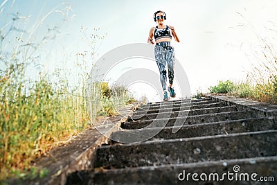 Middle-aged woman running downstairs and listening to music using wireless headphones and smartphone. Morning outdoor run training Stock Photo