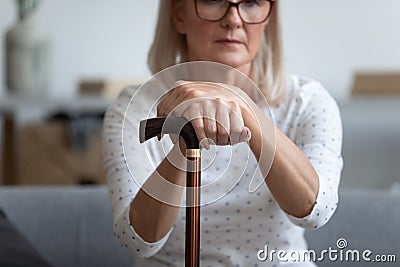 Middle-aged woman seated on couch holding in hands cane Stock Photo