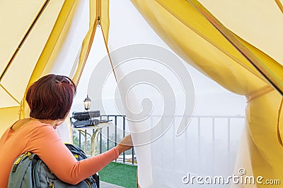 Middle aged woman sitting inside yellow tent looking at valley Stock Photo